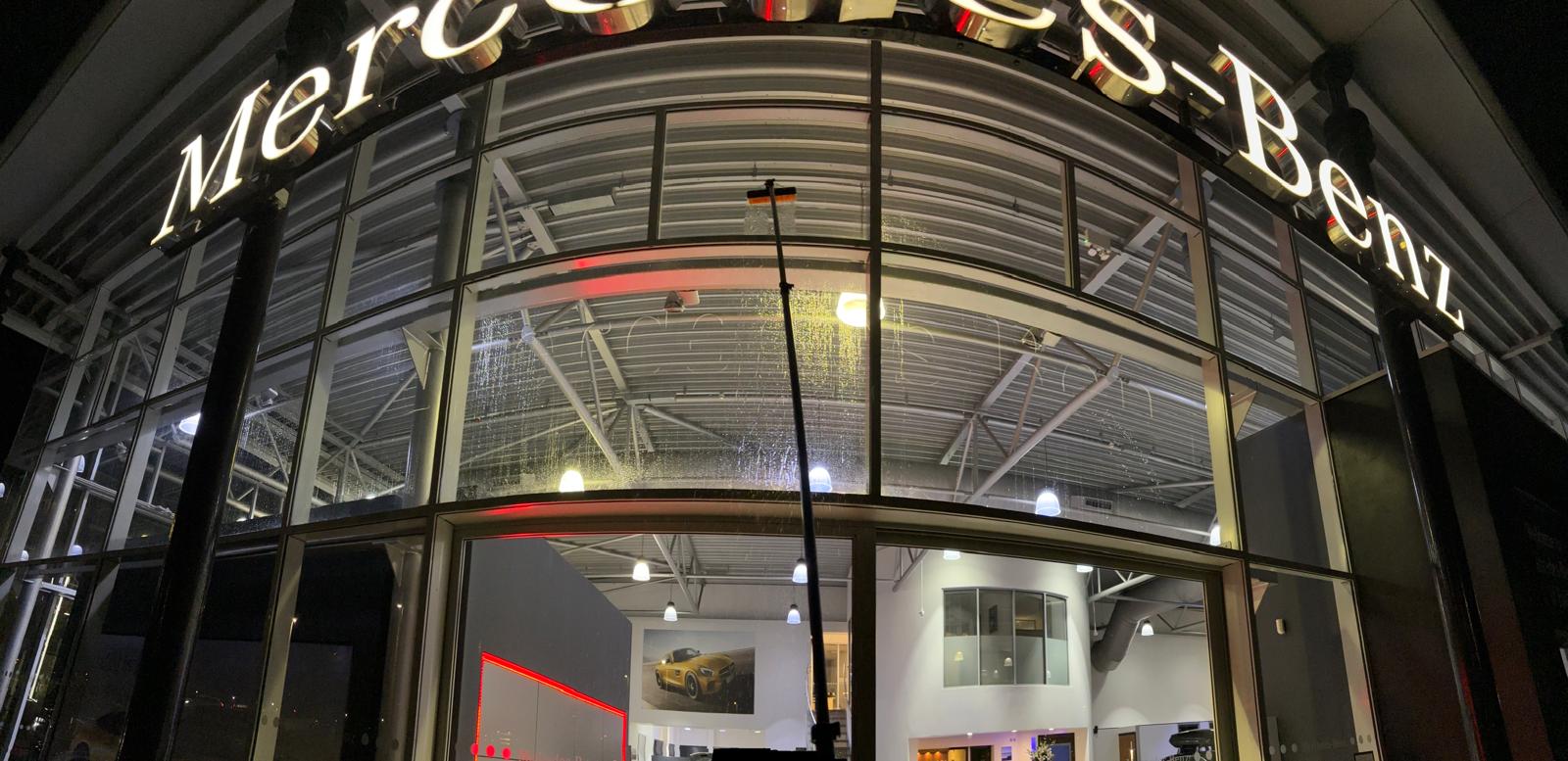 Water-fed pole cleaning the illuminated Mercedes-Benz showroom frontage at night