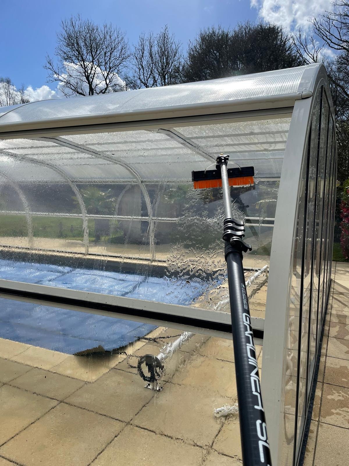Water-fed pole brush washing a swimming pool enclosure with pure water