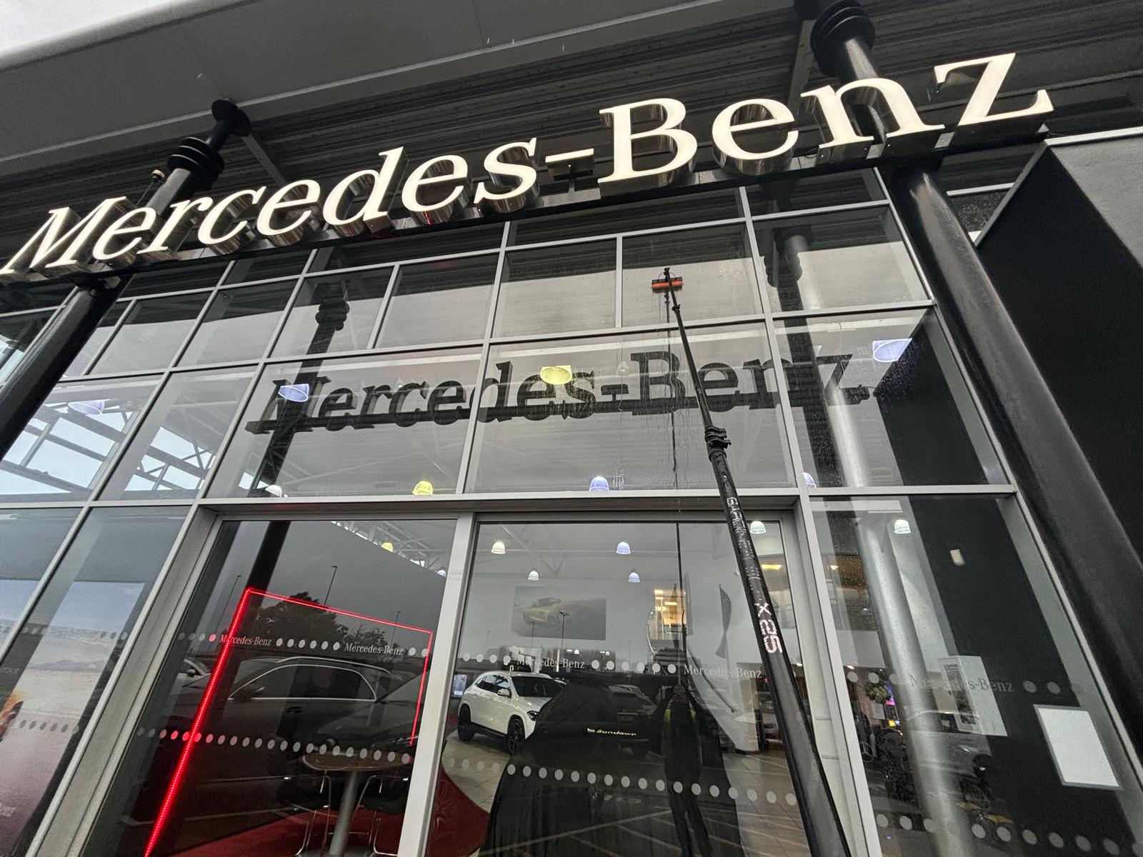 Water-fed pole cleaning the Mercedes-Benz dealership's tall glass frontage in daylight