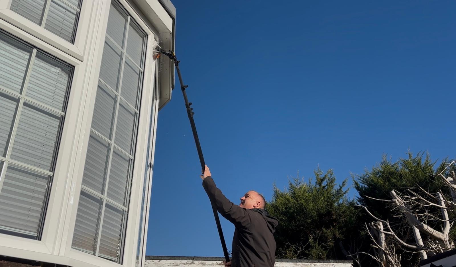 Andy using a reach pole to clean along the gutter and fascia line of a bay