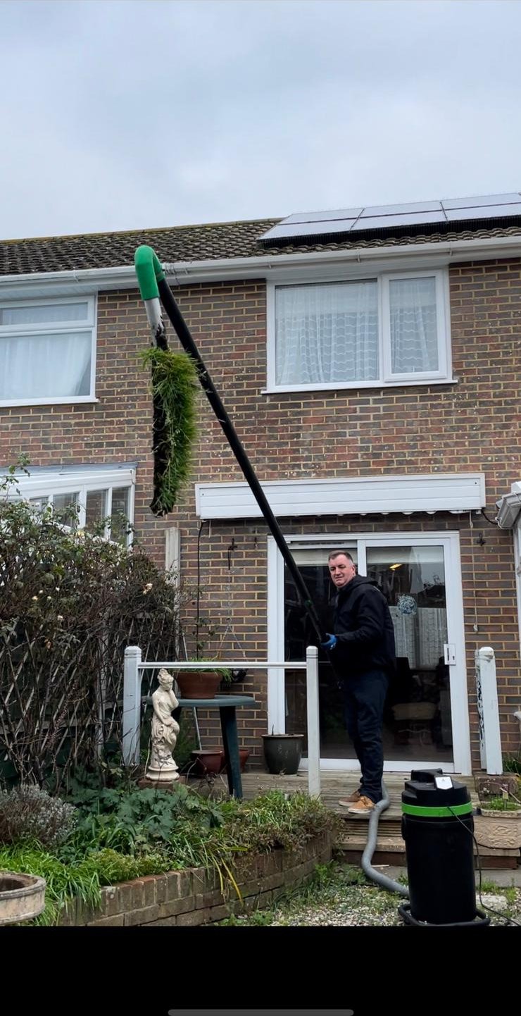 Gutter vacuum pole clearing leaves and moss from a house gutter