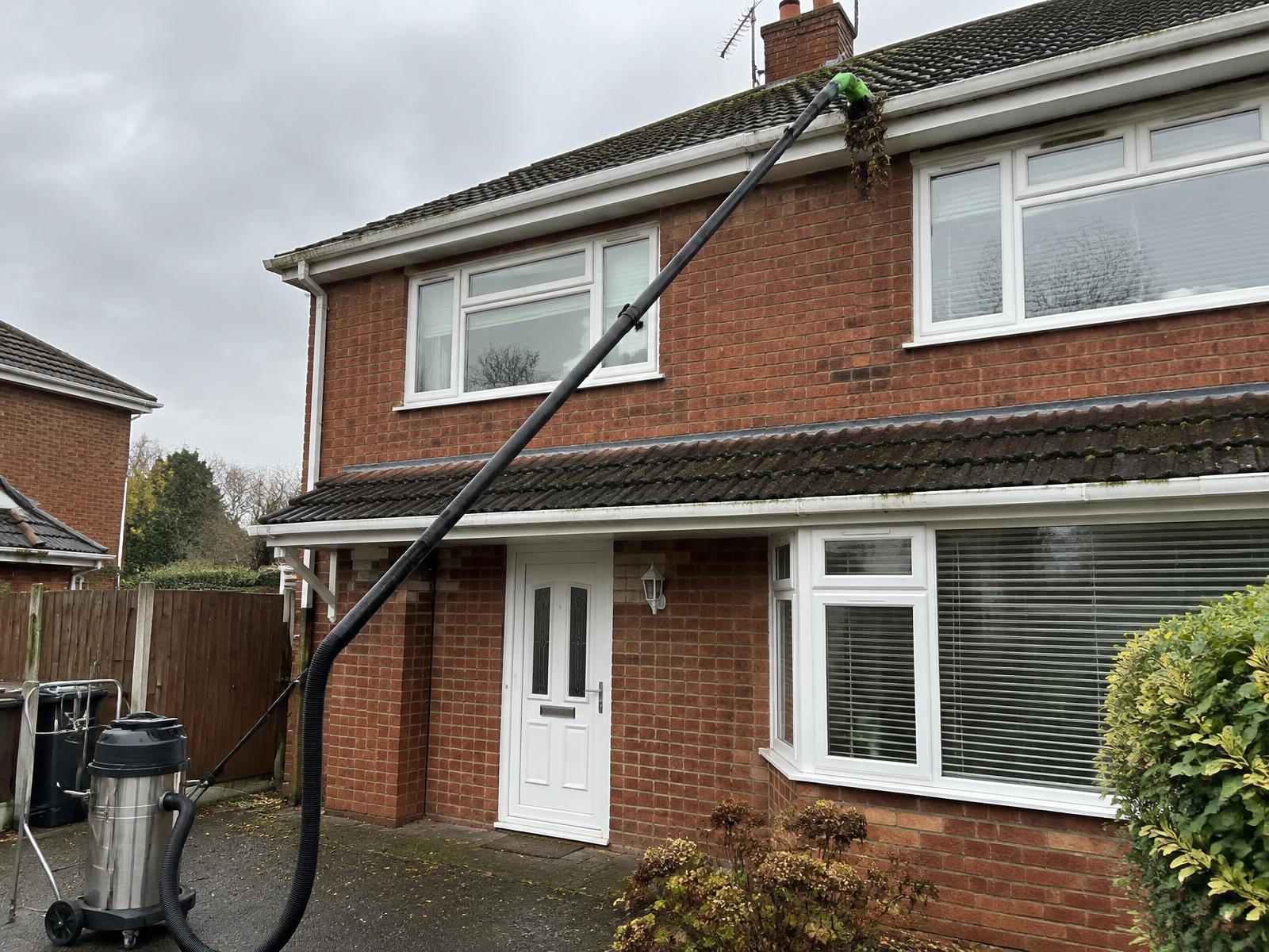 High-reach gutter vacuum pole clearing moss and leaves from the gutter of a brick house