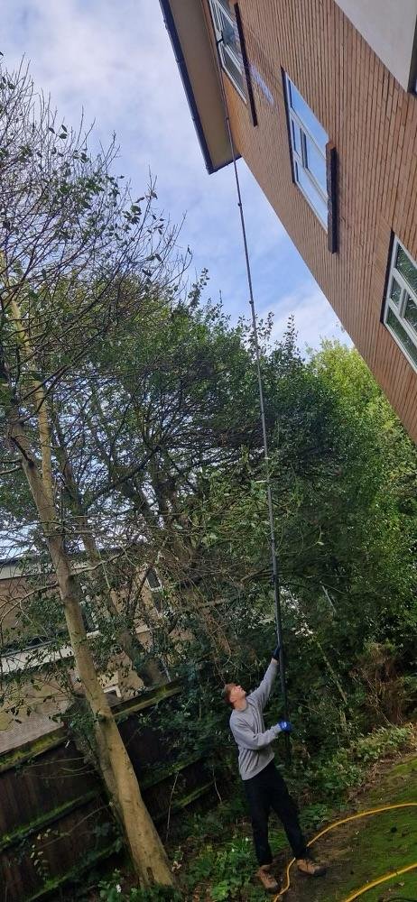 Andy using a water-fed pole to clean high upper-floor windows from the ground